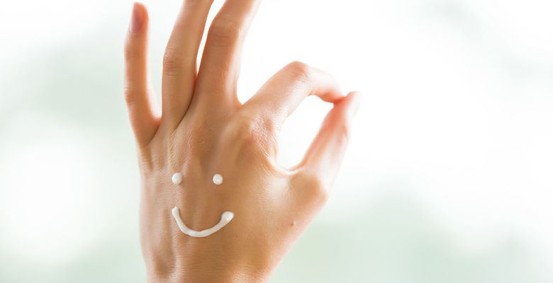 Gepflegte Hand, die mit einem Creme-Smiley glücklich aussieht Creme Smiley auf Hand, die "top" zeigt